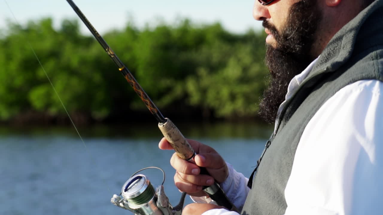 Close up, caucasian man with beard and sunglasses slowly winding in fishing rod, slow mo