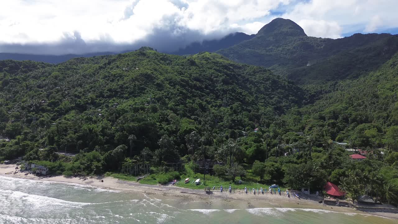 Filmagem aérea com drone de barcos ancorados na praia de Aninuan em Puerto Galera, Filipinas, com água cristalina, praia de areia, floresta densa e montanhas verdes no plano de fundo, formando uma paisagem tropical