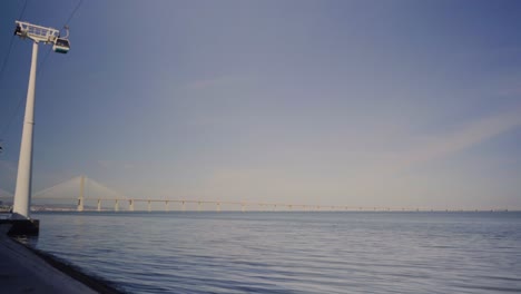 Städtischer-Stadtpark-Fluss-Seeufer-Wasserbrücke-Vasco-Da-Gama-Wind-Sonne-Sonnenuntergang-Blauer-Himmel-Seilbahn-Sessellift-Tejo-Portugal-Expo98-Steady-Shot-4k