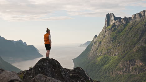 hiker on a mountaintop overlooking a fjord in lofoten, norway