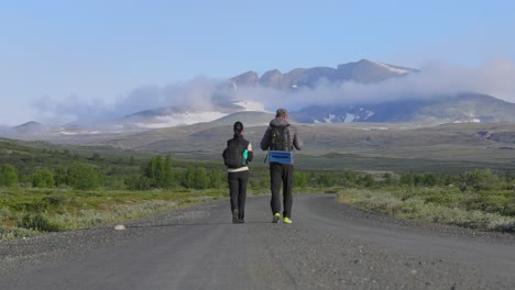 pareja de senderismo con mochilas en una carretera con montañas en el fondo. dovrefjell sunndalsfjella parque nacional es un parque nacional en noruega. hermosa naturaleza paisaje natural de noruega.