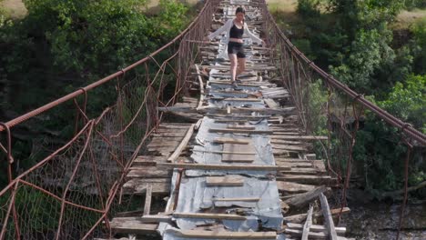 young asian girl cautiously crossing a wooden suspension bridge in poor condition