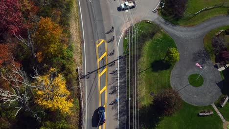 A-high-angle-aerial-view-over-a-country-road-with-colorful-trees-on-both-sides-on-a-sunny-day-in-autumn