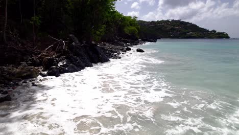 beautiful surreal aerial wide shot of water crashing on rocks and the beach shore sand buildings on hill in background blue sky white clouds turquoise water relaxation vacation tourism