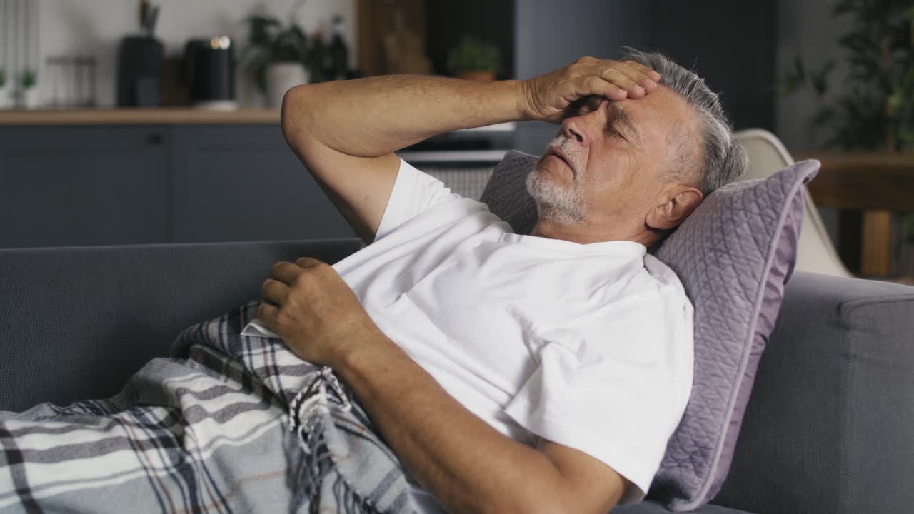 un caucásico mayor acostado en el sofá con resfriado y gripe.