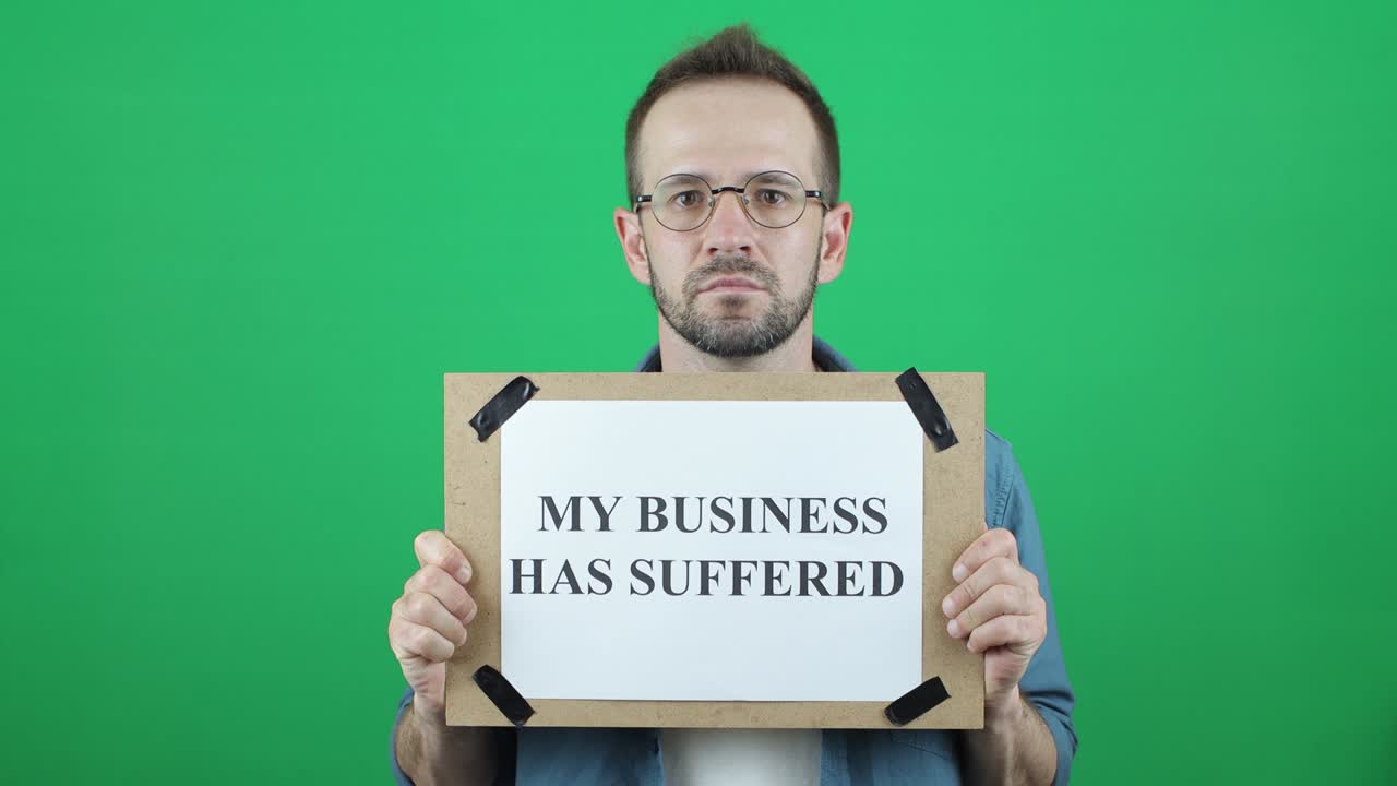 "그는 ""내 사업은 고통받았다""는 글이 적혀있는 유럽인 외모의 활동가, 백인 남성, 녹색 배경에 ""나의 사업은 고통 받았다""는 발을 손에 들고 있다."