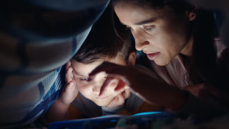 mother and child using tablet computer under blanket playing games on touchscreen technology little boy having fun before bedtime