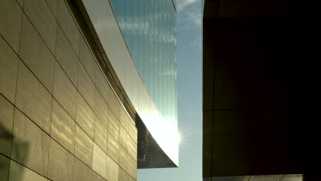 sunlight shines between modern buildings with reflecting glass and stone walls