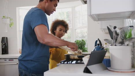 pre-teen african american girl and her father preparing food following a recipe on a tablet computer, close up
