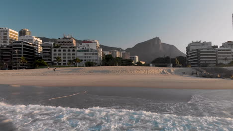 aerial approach of leblon beach in rio de janeiro at sunrise seen from the waves reaching the shore