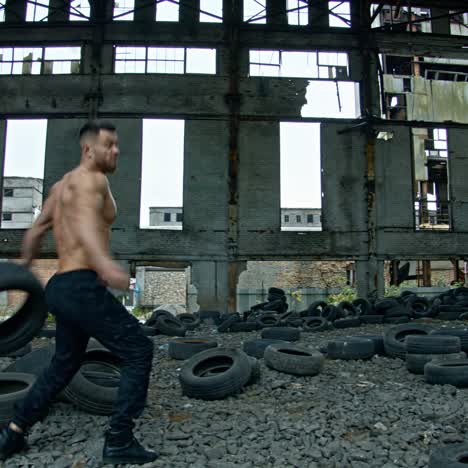 shirtless man training in ruined plant. strong athlete throwing old car tires while doing his workout in abandoned place. cross fitness routine.