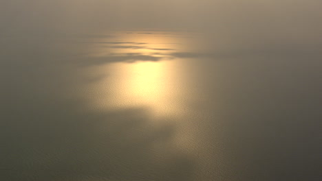 el sol poniente se refleja en el mar con algunos parches de sombra proyectados por las nubes