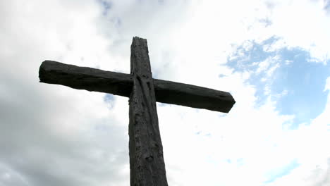 a cross in silhouette stands beneath swiftly moving clouds in a blue sky