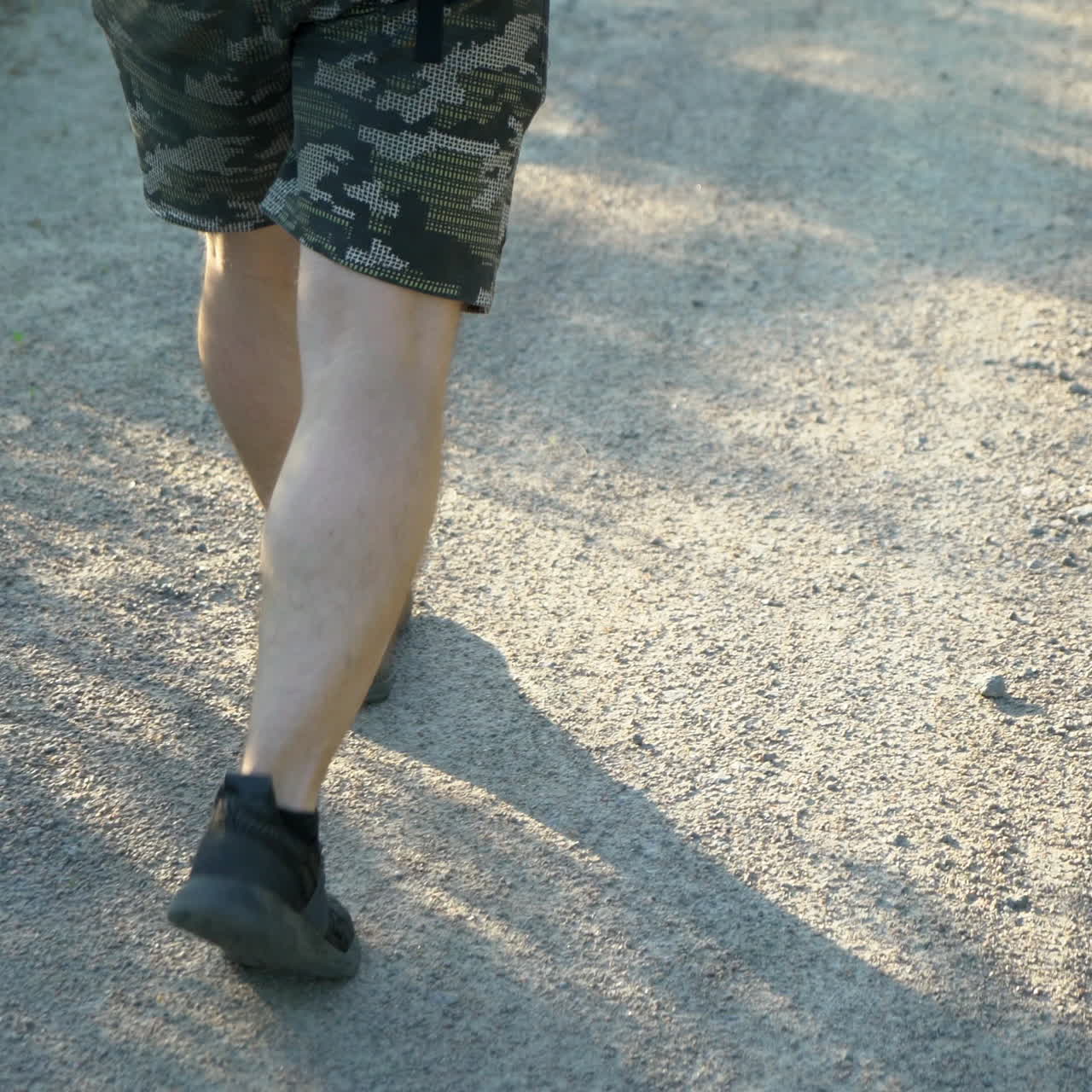 A man in shorts and black sneakers is walking on a dirt road on a summer day. A tourist goes hiking.