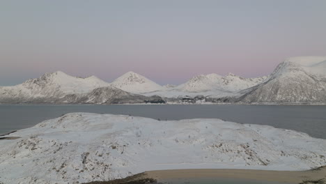 drone pullback reveals snowy island in fjord with stark white mountains