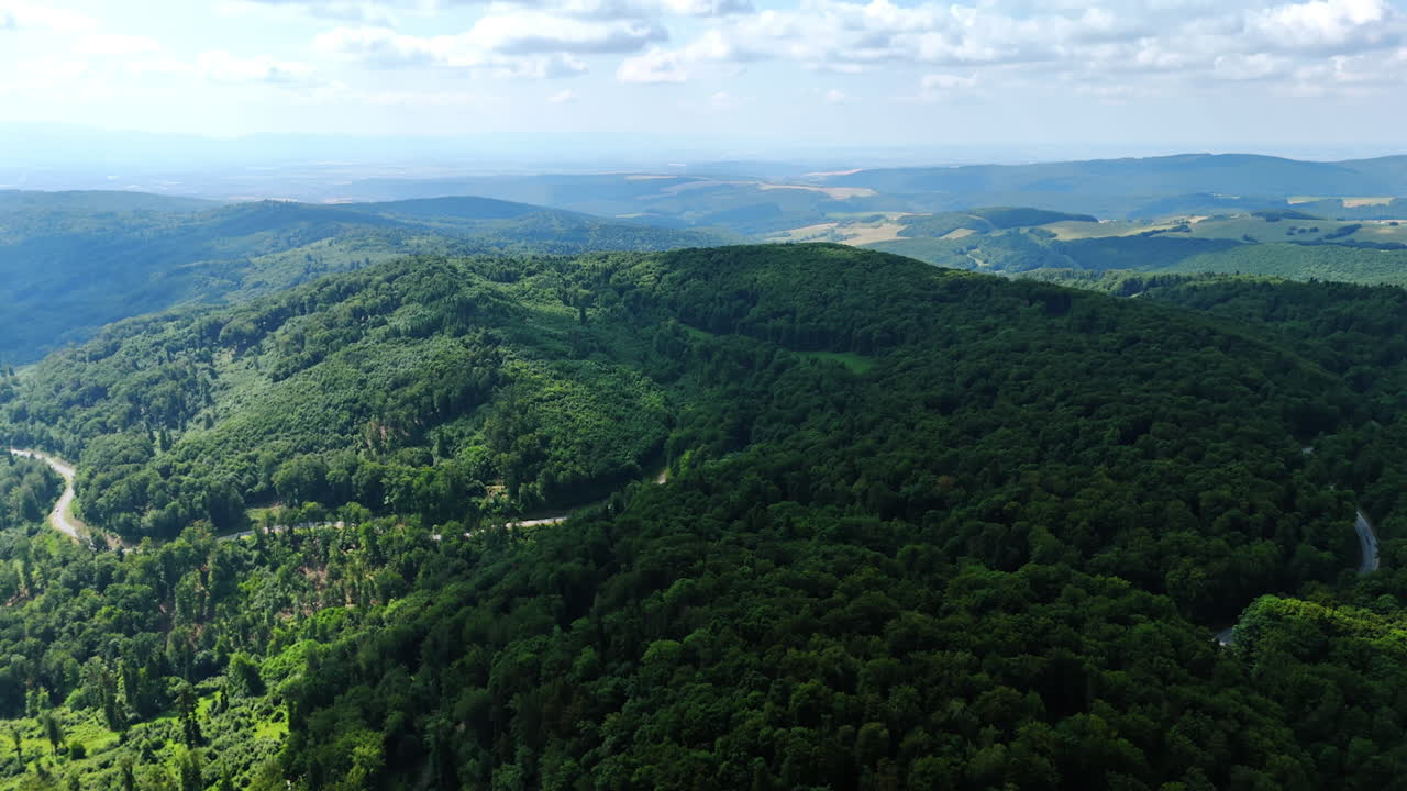 Lush green hills under a clear sky. Aerial view of lush green hills and distant mountains on a sunny day, showcasing nature's beauty