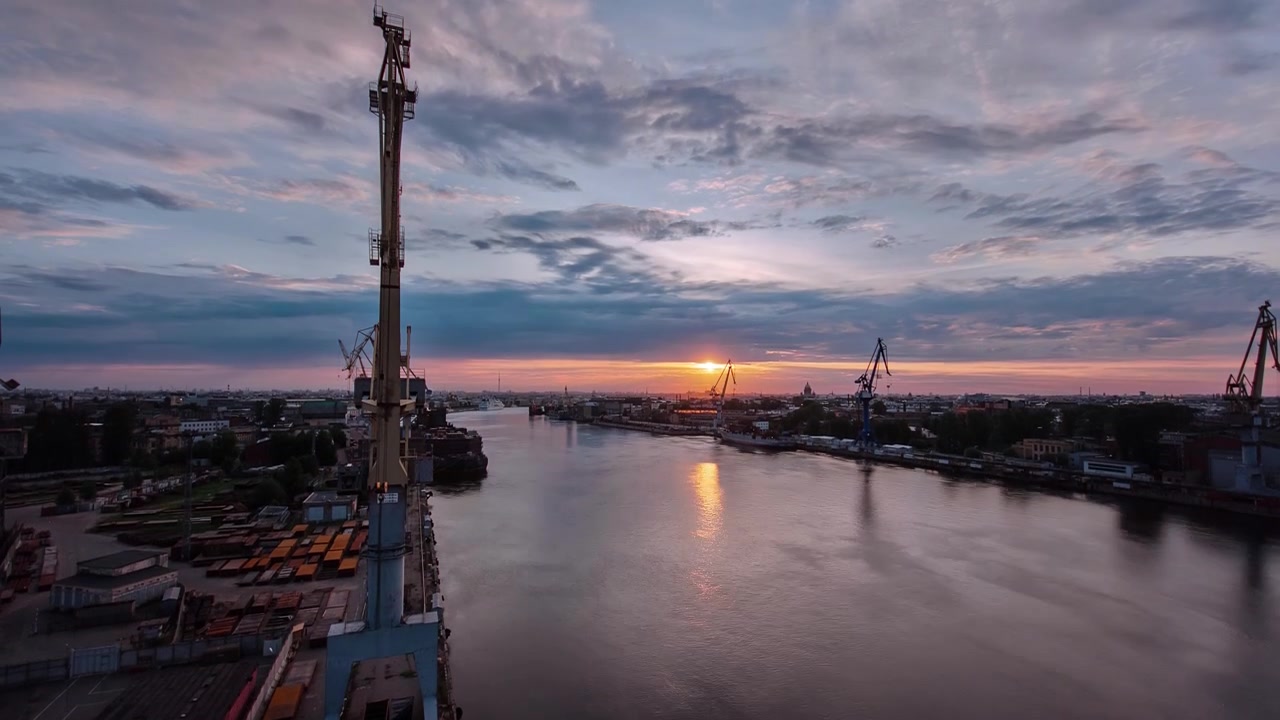 Skeppsvarv med historiska kranar i den industriella delen vid en flod under soluppgången i flygfoto i timelapse. Anläggningar och fabriker runt omkring. Färgglad himmel på morgonen.