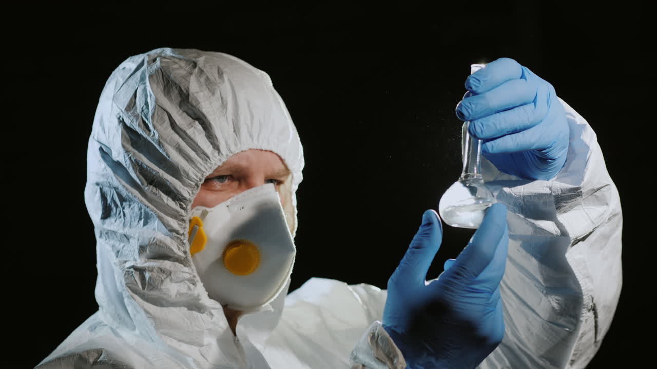 보호복과 인공호흡기를 입은 남자가 플라스크를 검사한다