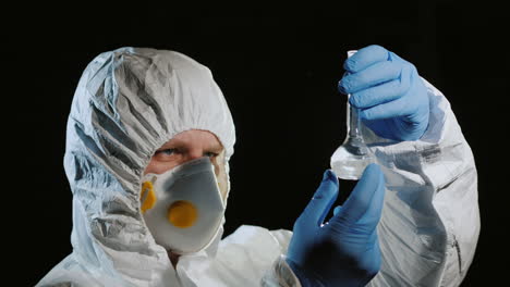 A-man-in-a-protective-suit-and-a-respirator-examines-a-flask