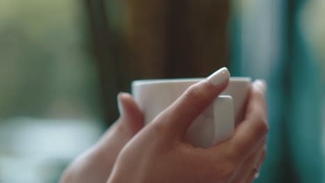 girl is holding a cup of coffee with her hands while in a cafe close-up