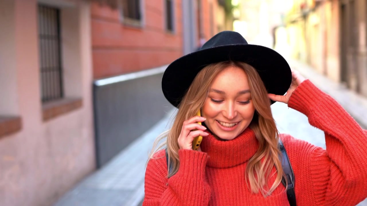 Blond kvinne snakker i smarttelefonen sin mens hun går nedover gaten.