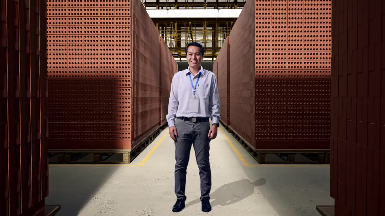 Full Body Of An Asian Male Professional Worker Standing With Red Brick Packed in Stacks Are Stored, He Look At The Camera And Smiling