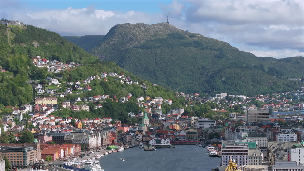 Drone pushing out from the historic Bryggen district, revealing boats, harbor, and mountain backdrop