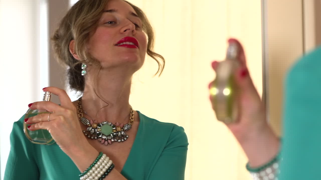 Donna con vestito turchese che si mette il profumo davanti a uno specchio