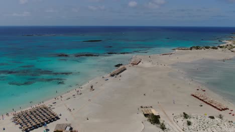 Elafonissi-Beach-with-sunshade-parasols-in-Crete-Greece-with-bathers-on-the-shores,-Aerial-dolly-in-shot