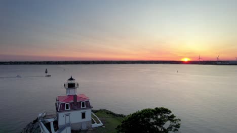 Aerial-view-of-the-Pomham-Rocks-Lighthouse,-an-orange-sunset-on-the-horizon