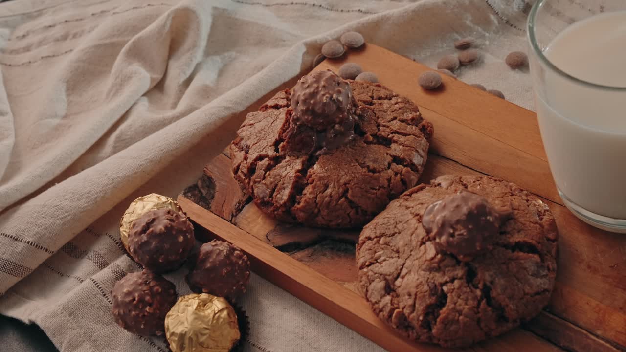 Primo piano di biscotti al cioccolato con confettini su un tagliere di legno e latte al chiuso.