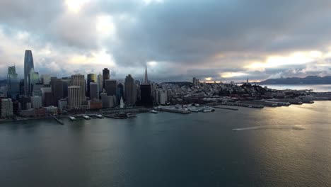 Imágenes-Aéreas-De-Drones-De-4k-30fps-Del-Horizonte-De-San-Francisco:-Un-Bote-Pequeño-Atraviesa-El-Agua-De-La-Bahía-De-Sf-Mientras-La-Puesta-De-Sol-Se-Refleja-En-Las-Olas-Tranquilas,-La-Hermosa-Arquitectura-Del-Horizonte-De-La-Ciudad,-El-Cielo-Cambiante-Del-Noroeste-Del-Pacífico-Pnw