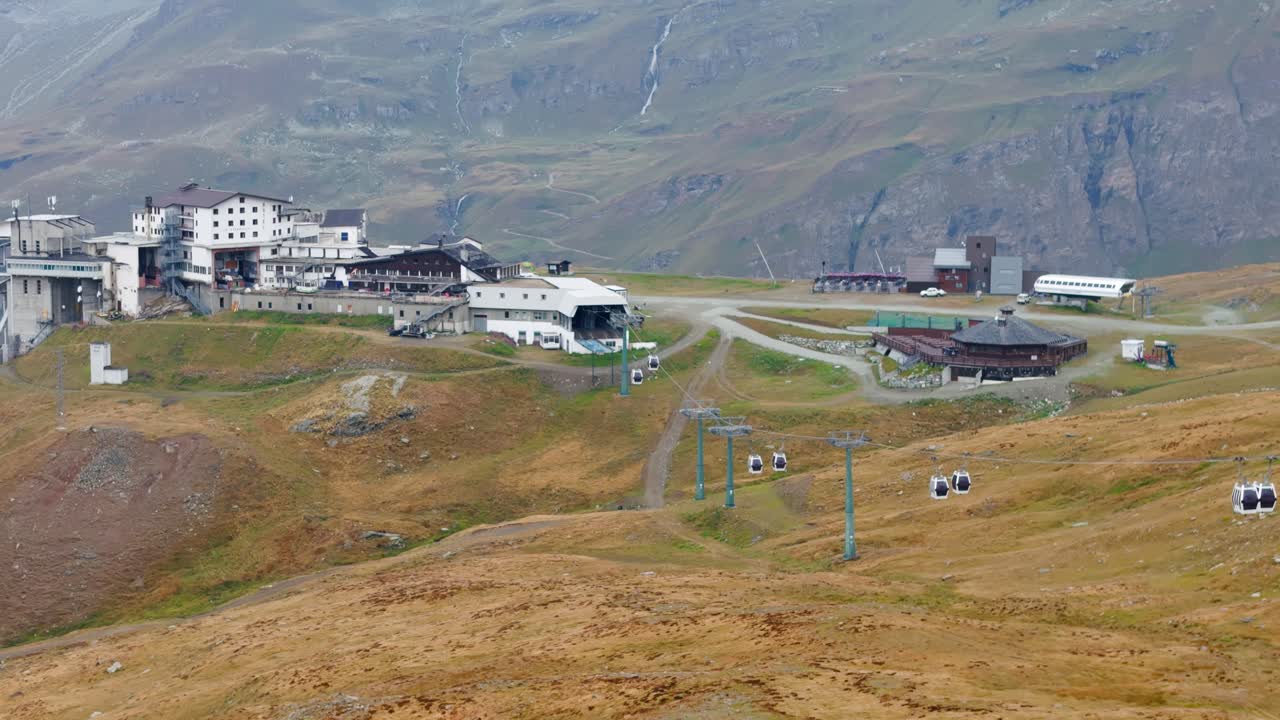 Ripresa aerea con drone che si avvicina a delle funivie che arrivano e partono da un resort montano a Cervinia, in Italia, circondato da spettacolari cime alpine e un paesaggio mozzafiato