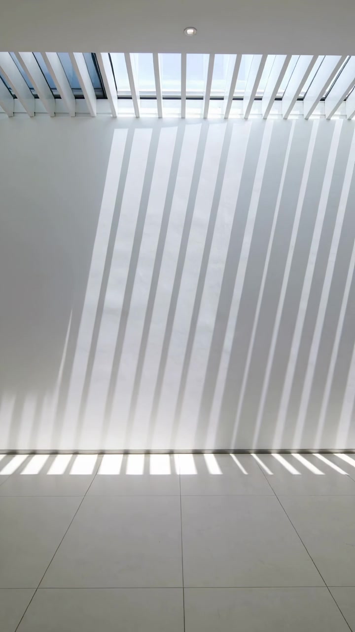 Video verticale: Fasce di luce solare in movimento che scivolano lungo una parete bianca e piastrelle in corridoio da un lucernario