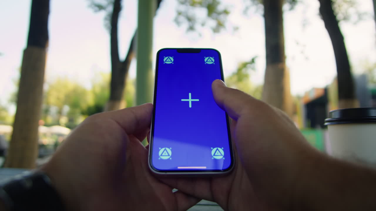 Young woman holding and swiping phone chroma key screen in the park in front of trees close-up. Girl with green screen on smart phone. Nature