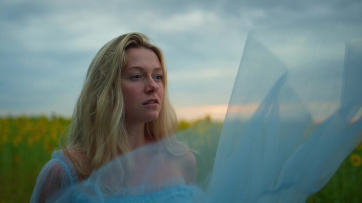Young Woman in Blue Dress Standing in Sunflower Field at Sunset