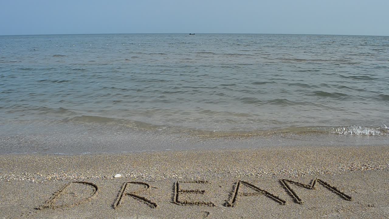 Inscription Dream on sea beach sand, with the wave. Shooting on the beach