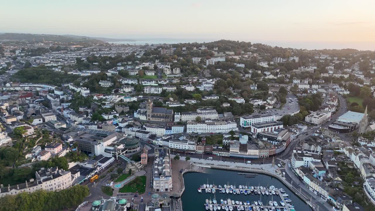 Cinematic aerial drone pull out revealing shot over Torquay showcasing city marina waterfront buildings and coastal landscape in Devon England
