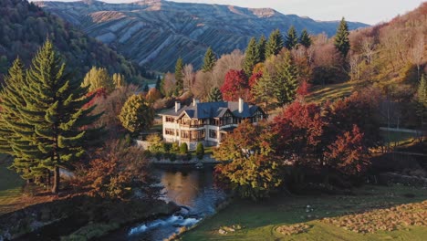 Aerial video captures a rustic mansion surrounded by autumn trees and a flowing river, set