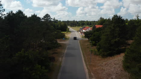 Forwards-tracking-of-car-driving-on-road-through-small-village.-Cyclists-with-dog-riding-on-cycling-path.-Denmark