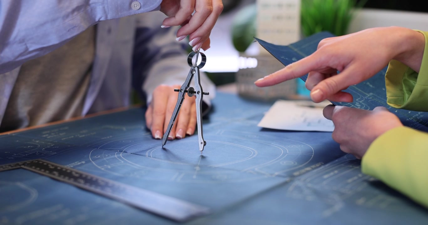 Woman designer draws circle on blueprint as colleague checks plan