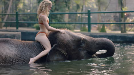 hermosa mujer montando un elefante en el zoológico jugando en la piscina salpicando agua turista mujer divirtiéndose en vacaciones exóticas en un santuario de bosque tropical