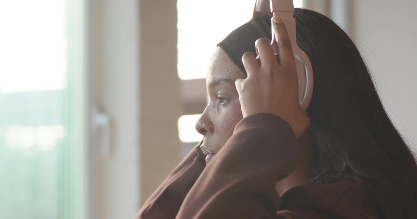 Mulher afro-americana no colchonete com faixa, olhando o celular, ajustando fones de ouvido rosa para ouvir.
