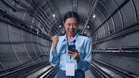 Asian Female With Her Smarphone In Underground Subway Tunnel, She Raises Her Fist Up With Screaming Goal