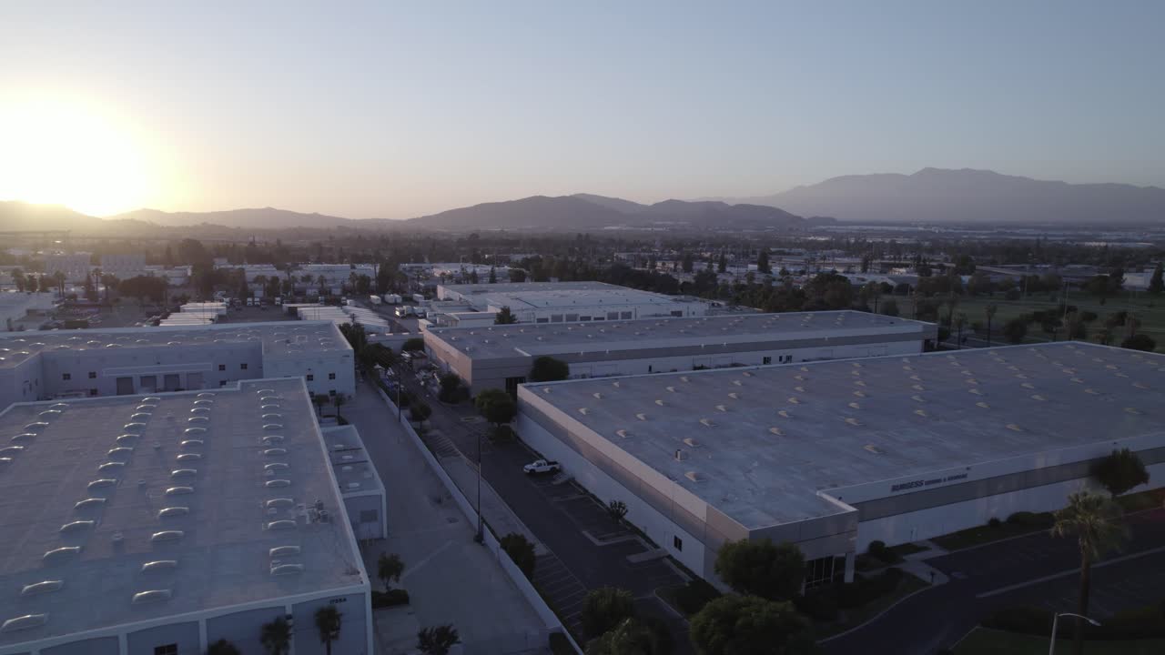 Mentre il sole tramonta, un drone plana con grazia su un paesaggio di magazzini commerciali, catturando la tranquilla bellezza del quartiere industriale nelle calde sfumature del cielo serale.