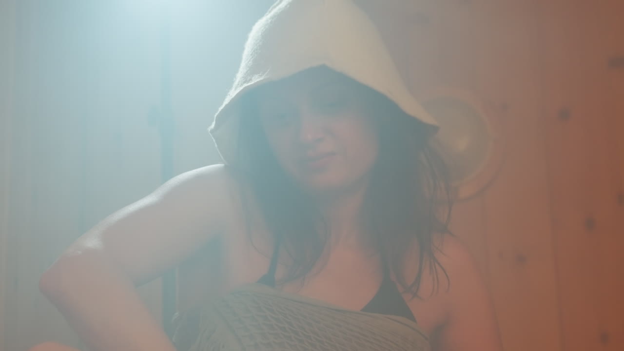 misty sauna scene with young woman spreading hydrating cream over shoulder and upper arm during serene wooden steam cabin self care ritual with gentle massage and relaxed expression