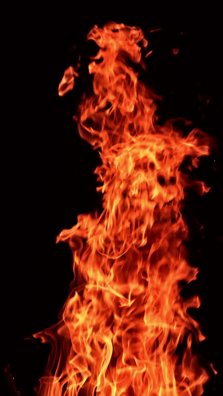 Long pillar of red flame going up into the air. Beautiful spots of sparkles flying from the fire. Black backdrop. Vertical video