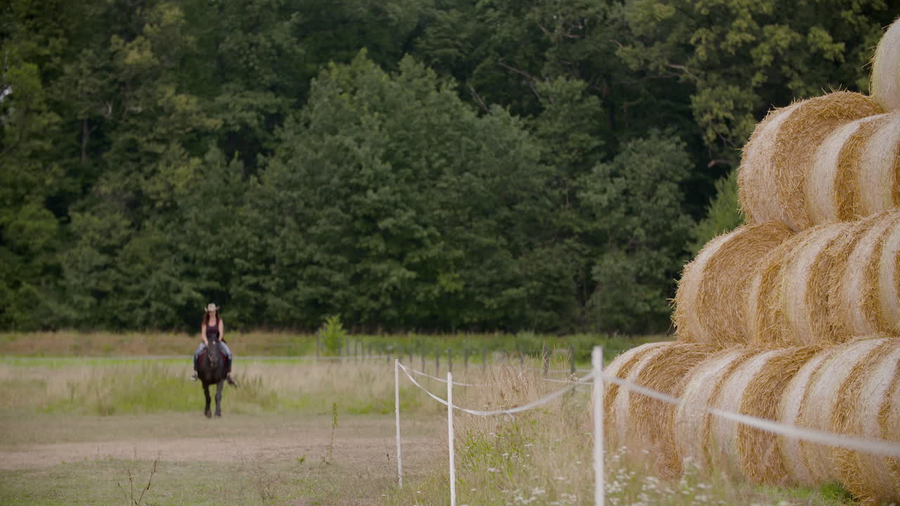 Woman horseback riding near hay bales