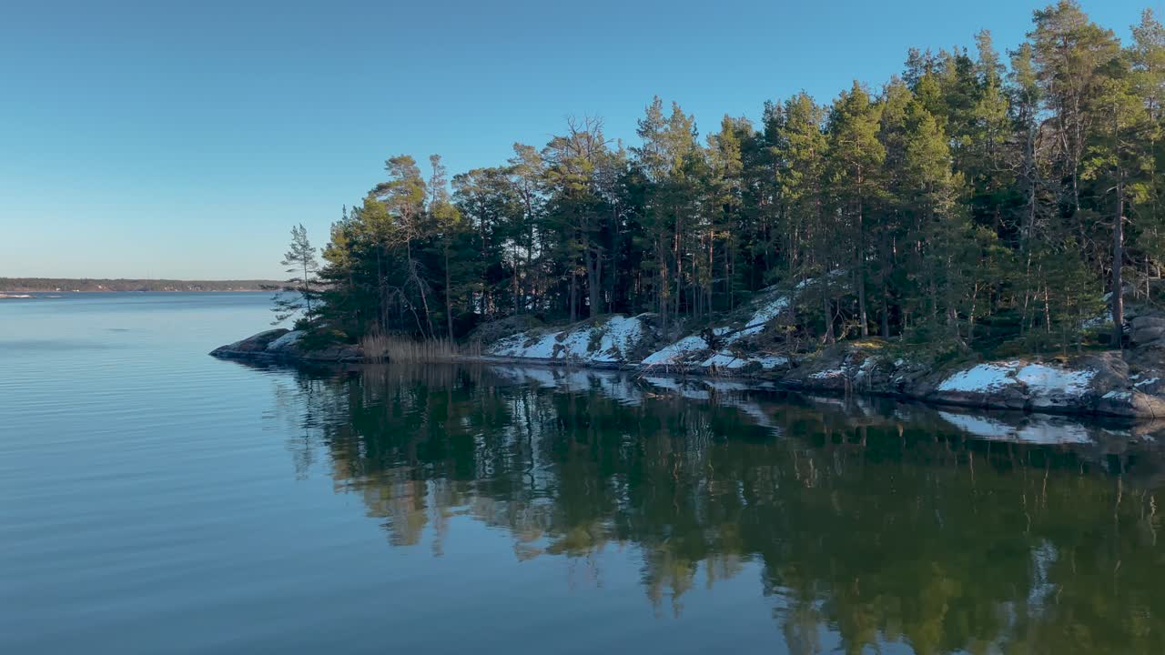 Stille vann i Stockholms skjærgård med furutrær og snøflekker, idyllisk naturmotiv.