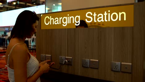 a woman is charging a smartphone on the charging station at the airport